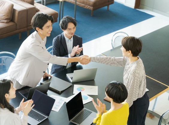 握手を交わすビジネスパーソンと拍手するメンバー