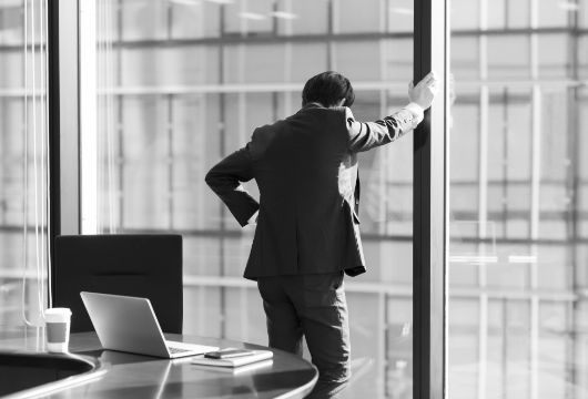 ビルのオフィスの窓際で片手をついて下を向くビジネスマン