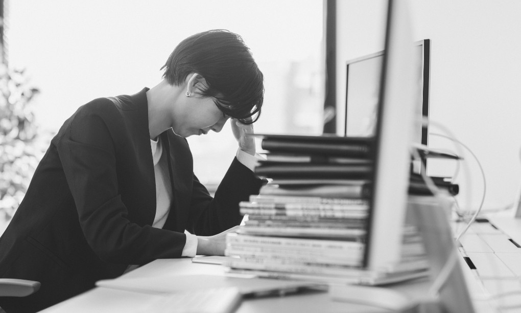 デスクで片手を手をおでこに当てて悩みこむ女性